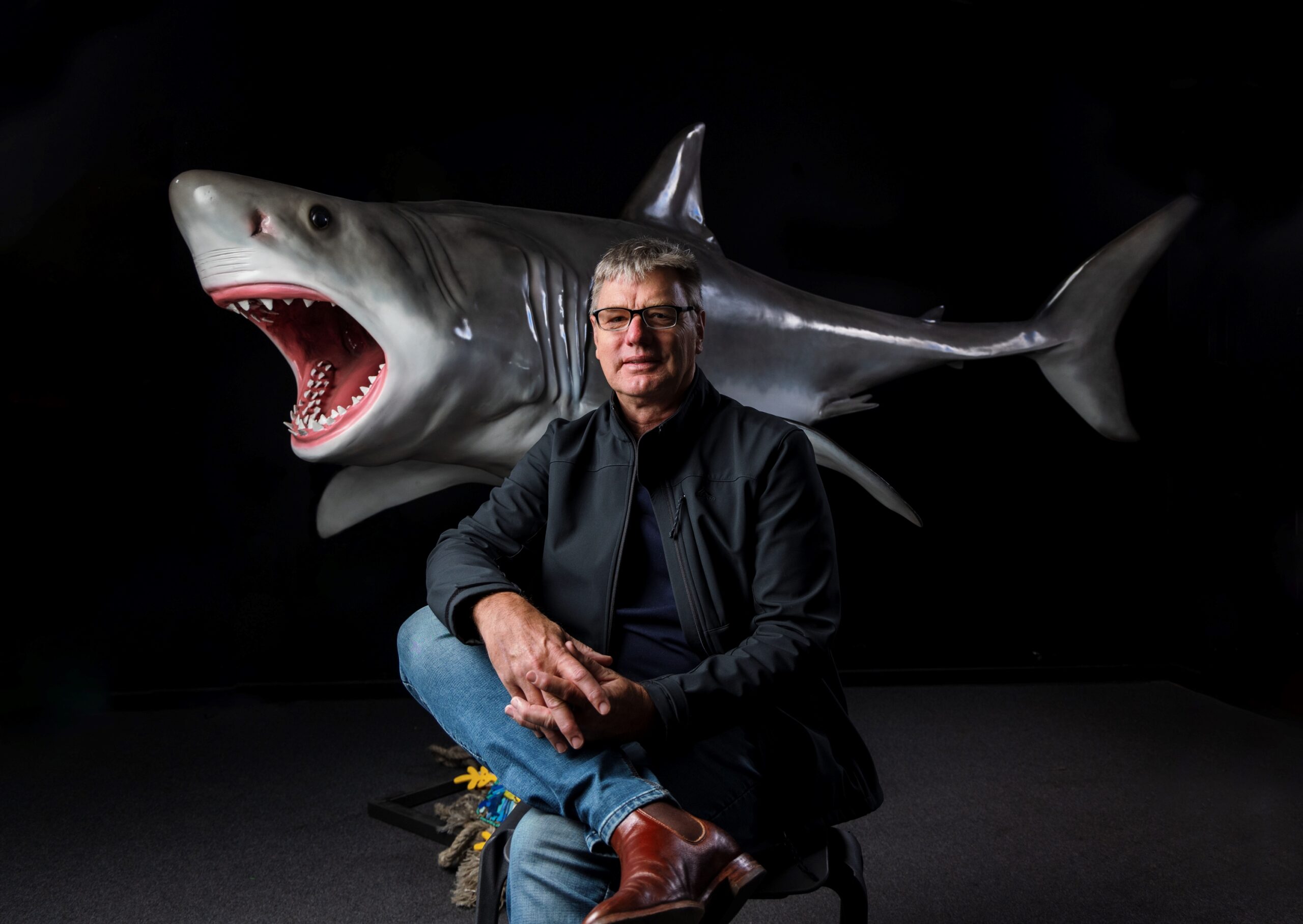 Photo of a man sitting in front of a model/design of a shark as part of a breakthrough announcement